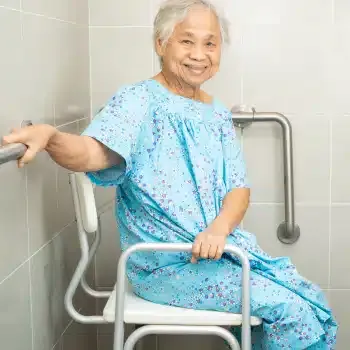 An older woman sitting on a shower chair beside a bathroom grab bar