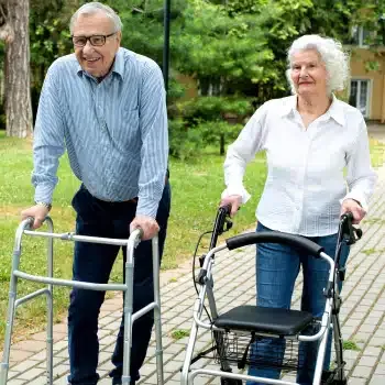 An older couple standing outdoors with a walker and a rollator