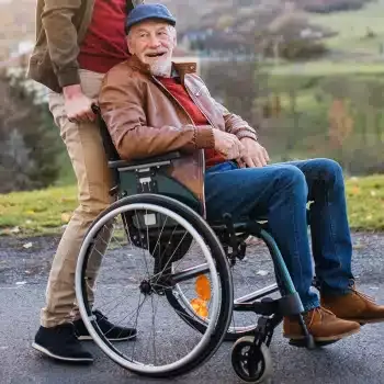 An older man smiling in a wheelchair while someone stands behind him